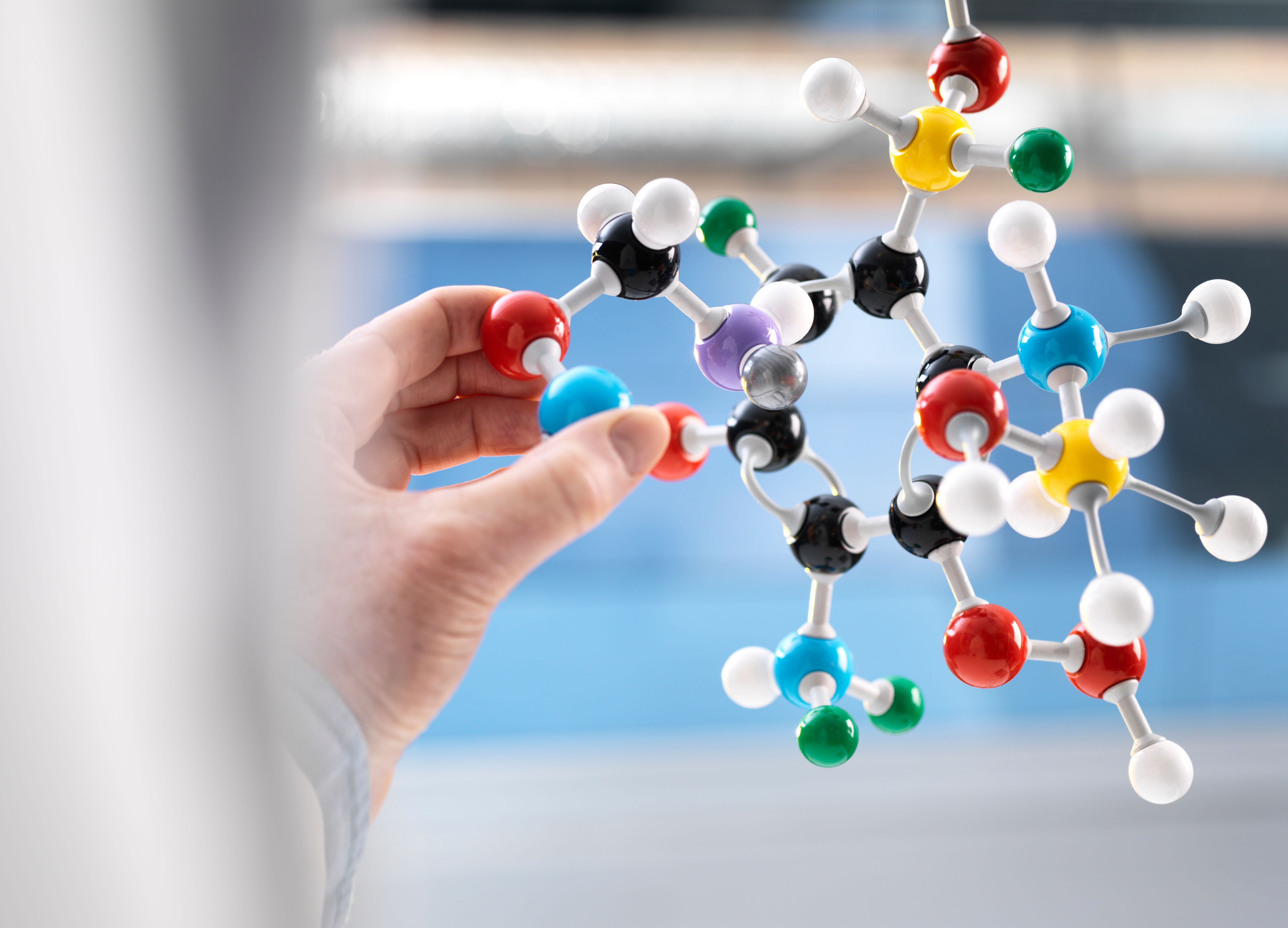 A scientist's hand holds a colorful molecular model against a laboratory backdrop