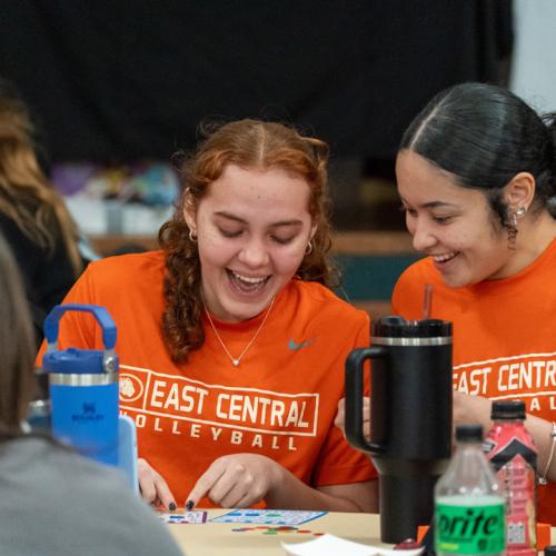 Two students laugh with each other while playing bingo.